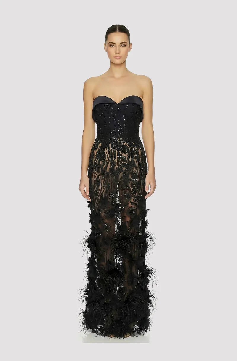 Front view of a woman in a Black corseted sheer column couture gown with a beaded bodice and skirt embellished with 3D floral appliqués and ostrich feathers 49, image 1
